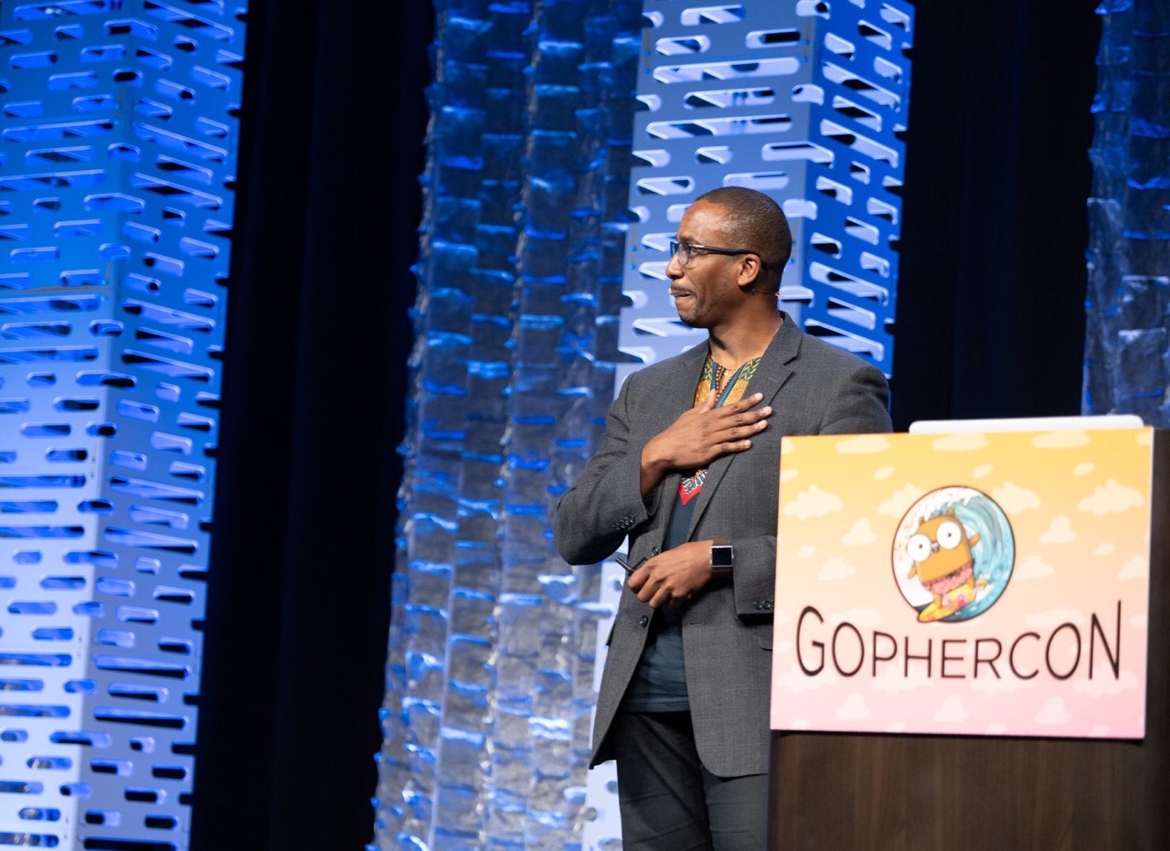Johnny at the GopherCon podium, hand on heart